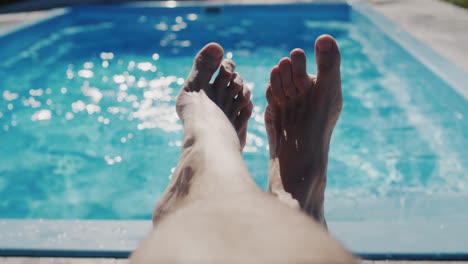A-man-is-relaxing-by-his-pool,-legs-are-visible-in-the-frame
