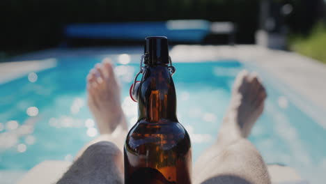 Ein-Mann-Entspannt-Sich-An-Einem-Heißen-Sommertag-Mit-Einer-Flasche-Bier-In-Der-Nähe-Seines-Pools.-Zeitlupenvideo