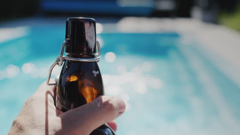 A-man-holds-a-bottle-of-beer-in-his-hand,-relaxes-by-the-pool-on-a-hot-day