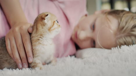 The-child-plays-with-a-ginger-kitten,-lies-on-the-floor-next-to-the-pet