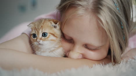 The-child-presses-his-cheek-against-the-ginger-kitten,-the-happy-owner-of-the-pet