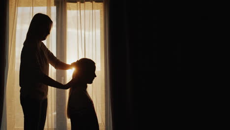 Silhouette-of-a-mother-combing-her-daughter's-hair-at-the-window