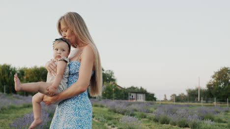 Attractive-mother-with-long-hair-holds-her-little-daughter-in-her-arms.-Standing-in-a-field-of-blooming-lavender