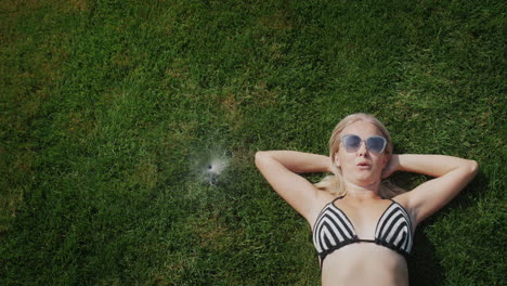 Attractive-woman-is-escaping-from-the-heat.-Lies-on-the-grass-near-the-fountain-of-water-from-automatic-watering