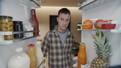 A-young-man-takes-a-container-with-breakfast-from-the-refrigerator.-View-from-inside-the-refrigerator