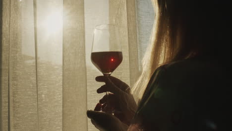 Bei-Sonnenuntergang-Steht-Eine-Frau-Mit-Einem-Glas-Wein-Am-Fenster