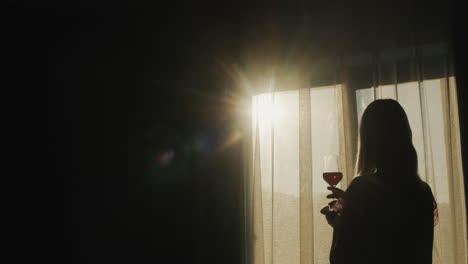 Bei-Sonnenuntergang-Steht-Eine-Frau-Mit-Einem-Glas-Wein-Am-Fenster