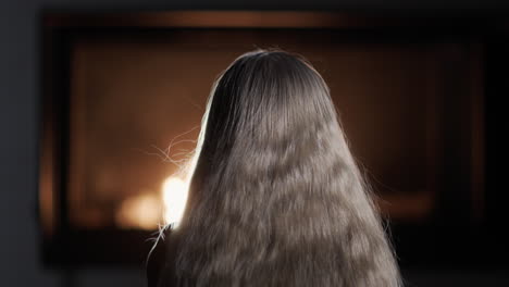 A-young-girl-with-long-hair-watches-the-fire-burn-in-the-fireplace