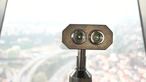 Coin-operated-binoculars-looking-out-over-city-buildings