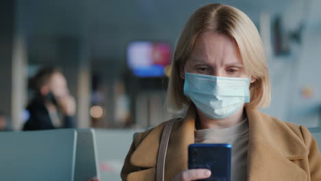 A-passenger-wearing-a-mask-in-the-airport-lounge.-Uses-a-smartphone