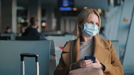 Portrait-of-a-woman-in-a-protective-mask,-sitting-in-the-airport-terminal-waiting-for-the-flight
