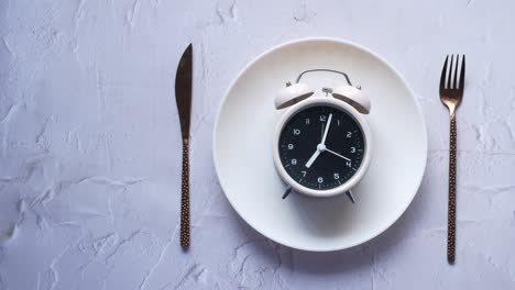 Alarm-clock-on-plate-on-wooden-table,-top-view