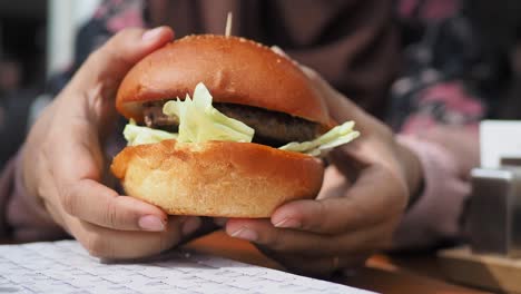 Hand-holding-beef-burger-on-table-close-up