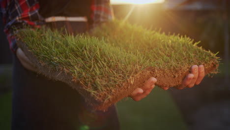 The-farmer's-hands-are-holding-a-piece-of-land-with-green-grass.-Land-trade-and-ecology-concept