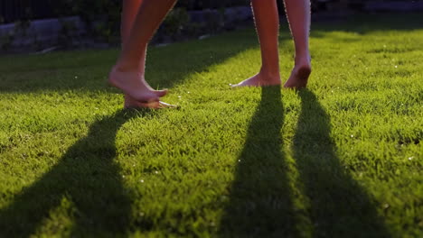 Two-barefoot-women-run-on-the-green-grass-in-jets-of-water.-Youth-and-health-concept