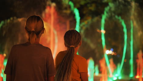 Mother-and-daughter-admire-the-fountain-with-lighting,-a-walk-through-the-evening-city