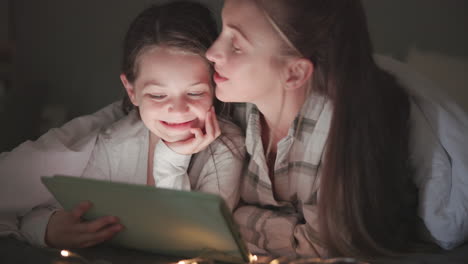 Tablet,-kiss-and-mother-with-daughter-in-bedroom