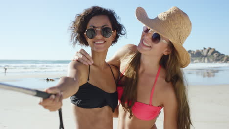 Two-friends-taking-selfies-on-the-beach-using-selfie-stick