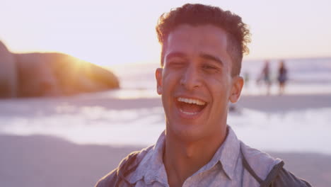 Portrait-of-attractive-man-smiling-on-beach-at-sunset-in-slow-motion