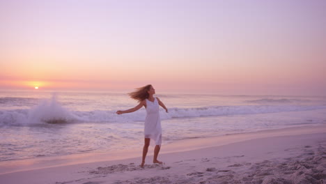 Free-happy-woman-spinning-arms-outstretched-enjoying-nature-dancing-on-beach-at-sunset-slow-motion-RED-DRAGON