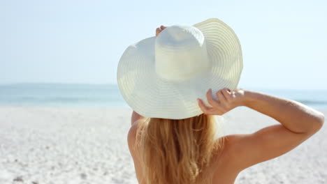 beautiful-young-woman-putting-on-sun-hat-at--beach-wearing-white-swimsuit