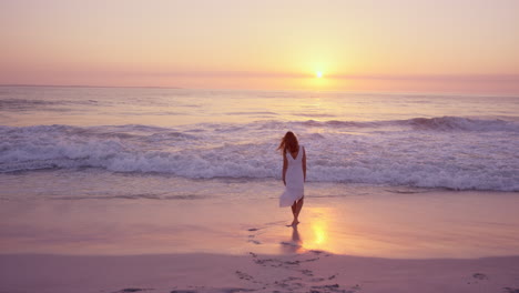 Schöne-Frau-In-Weißem-Kleid,-Die-Bei-Sonnenuntergang-In-Zeitlupe-Am-Strand-Entlang-Läuft,-Roter-Drache