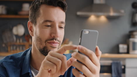 Attractive-man-at-home-using-smart-phone-in-kitchen-sending-message-on-social-media