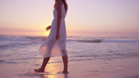 Schöne-Frau,-Die-Ein-Weißes-Kleid-Hochhebt-Und-Bei-Sonnenuntergang-In-Zeitlupe-Am-Strand-Entlang-Läuft,-Roter-Drache