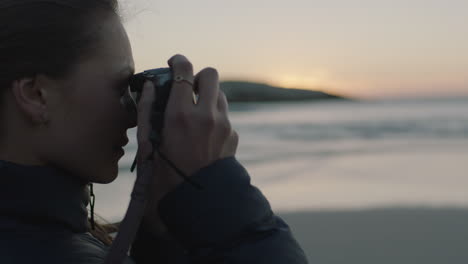 close-up-of-young-woman-photographer-on-beach-taking-photo-of-seaside-ocean-at-sunset-using-camera