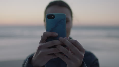 close-up-portrait-of-young-woman-taking-photo-using-smartphone-mobile-camera-technology-on-calm-seaside-beach-at-sunset