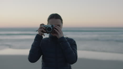 portrait-of-young-confident-woman-taking-photo-using-retro-camera-enjoying-calm-seaside-beach-at-sunset