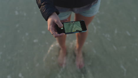 Nahaufnahme-Einer-Frau-Am-Strand,-Die-Mithilfe-Der-Smartphone-Kameratechnologie-Ein-Foto-Von-Wellen-Macht,-Die-Sanft-Ihre-Füße-Plätschern,-Und-Reiseerlebnisse-Teilt