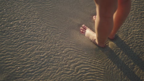 close-up-of-woman-feet-standing-on-sandy-beach-sea-water-flowing-gently-vacation-concept