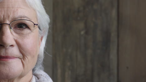 half-face-portrait-of-happy-elderly-woman-smiling-satisfaction-looking-at-camera-wearing-glasses-on-wooden-background