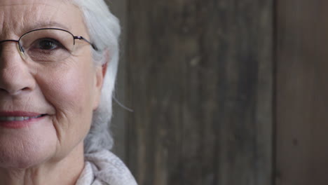 half-face-portrait-of-happy-elderly-woman-smiling-looking-at-camera-cheerful-wearing-glasses-on-wooden-background
