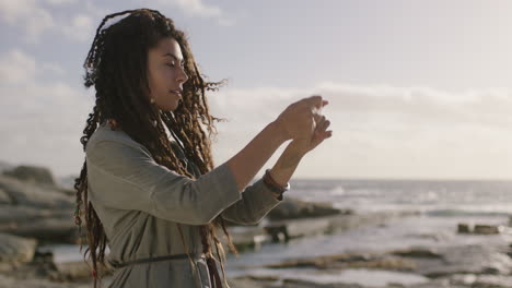 beautiful-mixed-race-woman-with-dreadlocks-taking-photo-at-beach-using-phone-smiling-happy