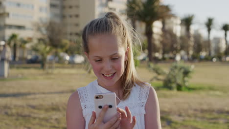 portrait-happy-little-blonde-girl-using-smartphone-enjoying-playing-mobile-games-smiling-cheerful-satisfaction-on-warm-sunset-park