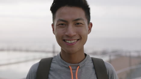 close-up-portrait-of-charming-young-asian-man-smiling-cheerful-optimistic-by-cloudy-seaside