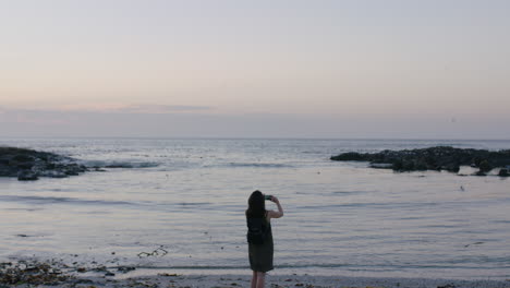 portrait-of-brunette-woman-on-beach-taking-photo-of-seaside-using-phone