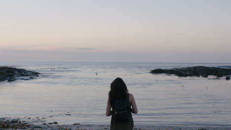portrait-of-brunette-woman-walking-on-beach-taking-photo-of-seaside-using-phone