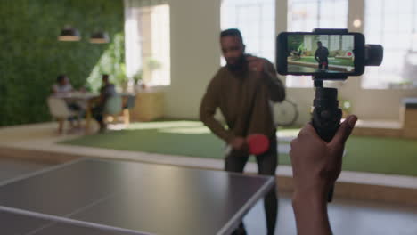 young-black-business-people-playing-ping-pong-in-office-enjoying-competitive-fun-colleague-using-smartphone-sharing-game-on-social-media-taking-video