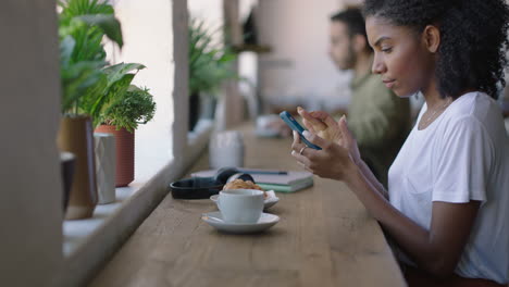 Feliz-Mujer-Afroamericana-Usando-Un-Teléfono-Inteligente-En-Una-Cafetería-Navegando-Mensajes-En-Línea-Disfrutando-De-Compartir-El-Estilo-De-Vida-En-Las-Redes-Sociales-Relajándose-En-Un-Restaurante-Cafetería
