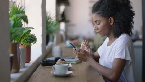 Glückliche-Afroamerikanische-Frau,-Die-Im-Café-Ihr-Smartphone-Nutzt-Und-Online-Nachrichten-Durchstöbert-Und-Ihren-Lebensstil-In-Sozialen-Medien-Teilt-Und-Sich-Im-Café-Restaurant-Entspannt