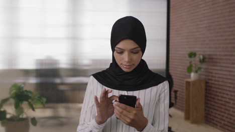 Porträt-Einer-Jungen-Muslimischen-Geschäftsfrau,-Die-SMS-Schreibt-Und-Mithilfe-Mobiler-Smartphone-Technologie-In-Einem-Geschäftigen-Büroarbeitsplatz-Surft