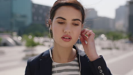 close-up-portrait-of-beautiful-middle-eastern-woman-smiling-happy-intern-listening-to-music-using-earphones-enjoying-sunny-windy-day-in-urban-city-background