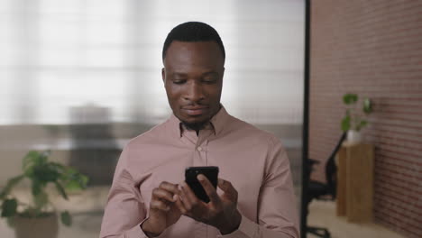 portrait-of-young-african-american-businessman-texting-browsing-using-smartphone-networking-app-in-modern-office-workspace