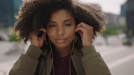 Primer-Plano-Retrato-De-Una-Joven-Estudiante-Afroamericana-De-Moda-Usando-Auriculares-Escuchando-Música-Sonriendo-Confiada-En-La-Cámara-Disfrutando-Del-Estilo-De-Vida-Universitario-Urbano
