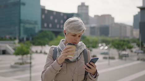 portrait-of-mature-caucasian-business-woman-texting-browsing-using-smartphone-social-media-relaxed-drinking-coffee-beverage-in-urban-city