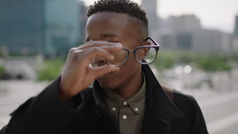 close-up-portrait-of-young-trendy-african-american-man-student-looking-serious-at-camera-confident-removes-glasses-in-city-background