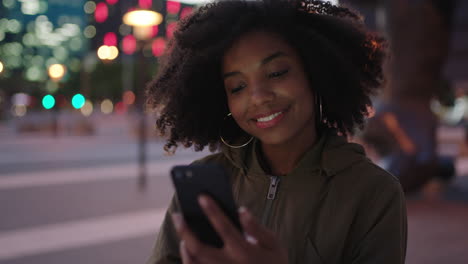 portrait-of-stylish-young-black-woman-with-afro-texting-browsing-using-smartphone-mobile-technology-in-city-at-night